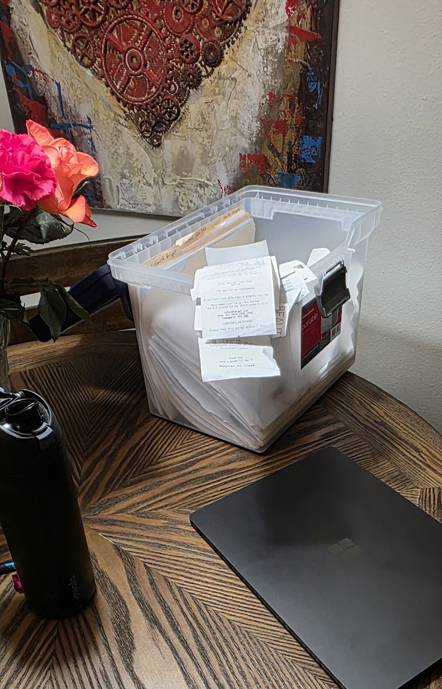 A bin overflowing with receipts and paperwork next to a closed laptop